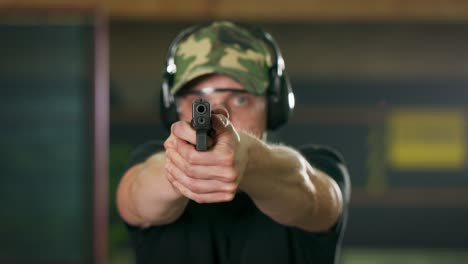 a shooting instructor wearing protective glasses and headphones aims at the camera at an indoor firing range