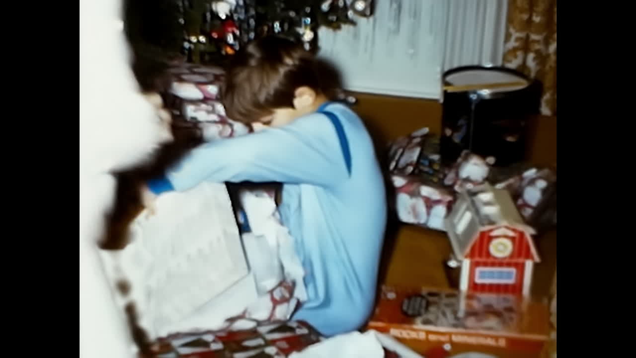 Boy in Blue Shirt Sitting in Front of Christmas Tree. CIRCA USA - 1970s: A young boy wearing a blue shirt sits in front of a Christmas tree in this 1970s video archive from the USA.