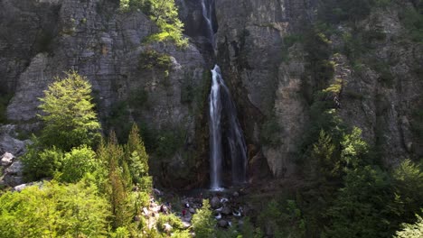 tourists visiting beautiful waterfall of theth, hiking on mountains in albanian alps