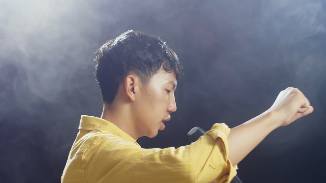 젊은 아시아 소년이 마이크를 들고 색 연기가 검은색 배경에 하는 가까운 측면 뷰