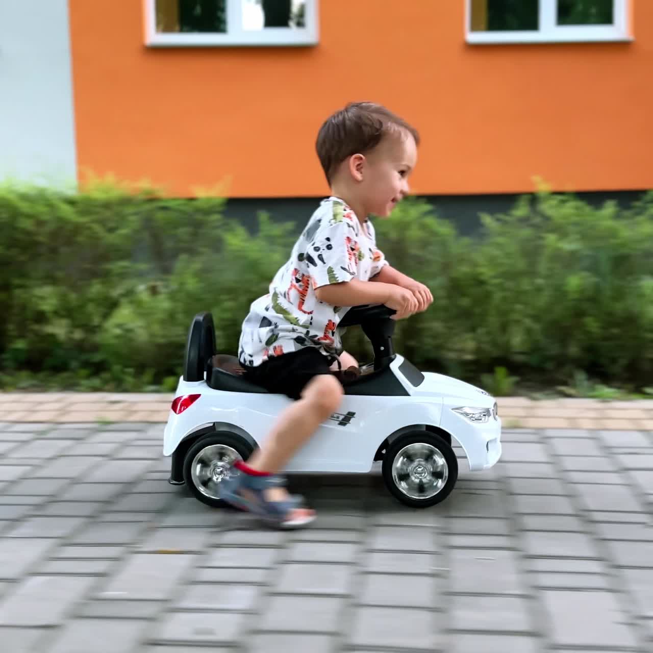 Bellissimo bambino che guida velocemente un'auto giocattolo. Bambino felice e in salute che si diverte all'aperto in estate