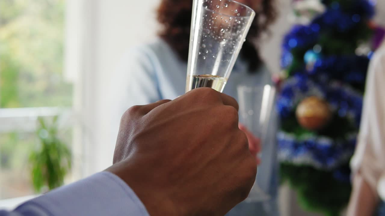 vista de cerca de las manos de un grupo multiétnico de trabajadores de oficina haciendo clic en copas con vino espumoso usando sombreros de navidad y