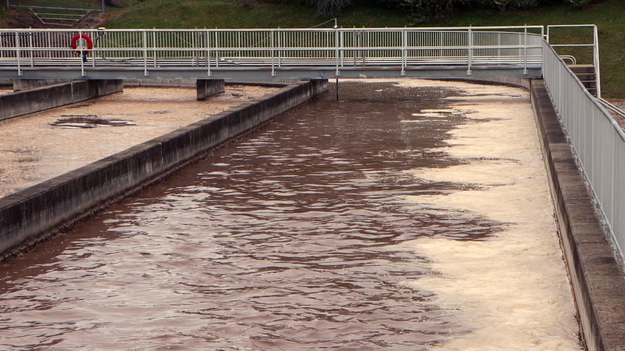Foaming brown wastewater swirls through an aeration basin, highlighting industrial treatment in action with bubbling, circulating liquid under controlled flow