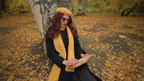 el turista en la soledad hojea las páginas del libro contemplativamente, sentado solo en la naturaleza, vestido con boina amarilla y silenciador, rodeado de hojas de otoño, inmerso en un momento de lectura pacífica