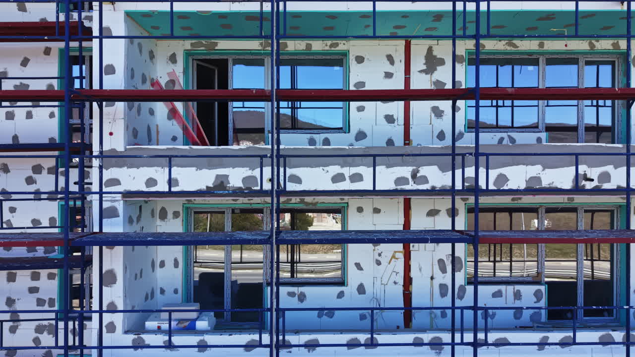 Construction site shows a building with scaffolding and plasterwork during the day with reflections in the windows