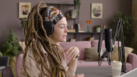 side view of woman with dreadlocks recording a podcast wearing headphones and talking into a microphone sitting at a desk