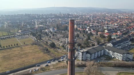 flying around a tall brick industrial chimney surrounded by a residential neighborhood with red-roofed houses. drone view of the cityscape.