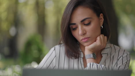 pensive woman brunette hispanic ethnic group sits at a table in a summer cafe with a laptop. serious business woman pondering problem solving and business development strategy