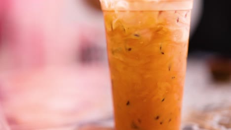 a close-up view of a thai iced tea in a clear cup with a vibrant, warm background