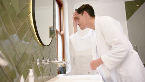 focused biracial man inspecting hair and face in bathroom mirror, copy space, slow motion