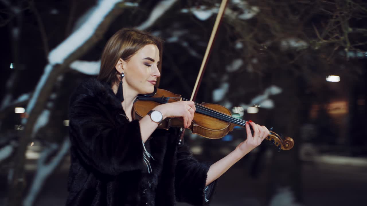 Musician playing on violin at night. Portrait of beautiful violinist playing at night winter street