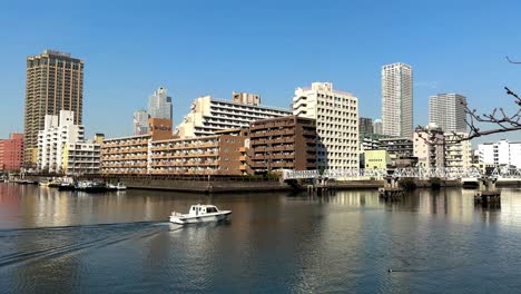 barco blanco navegando a lo largo de un río con paisaje urbano moderno, cielo azul claro, luz del mediodía, escena urbana frente al mar, toma estática