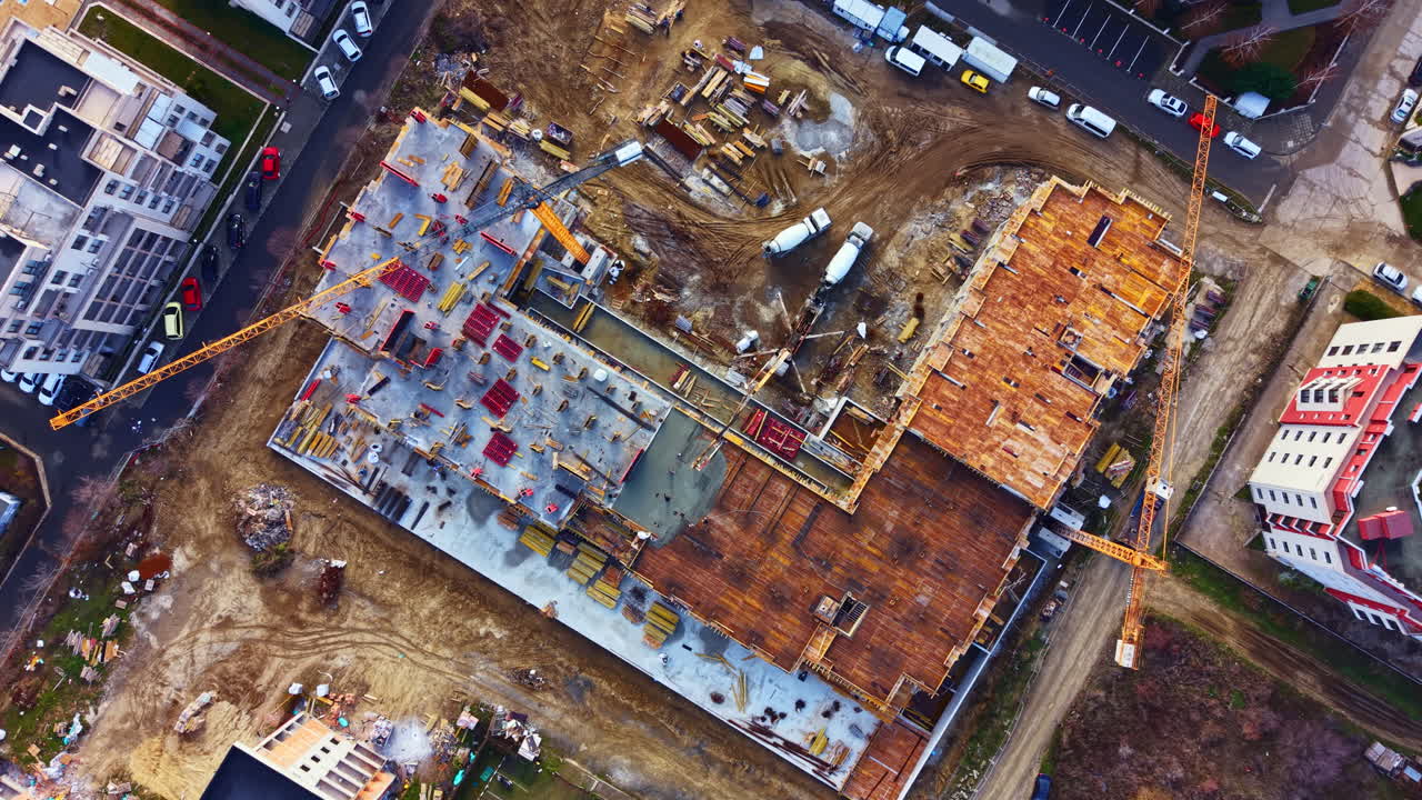 Construction site in progress with cranes, equipment, and building materials in the urban area at midday