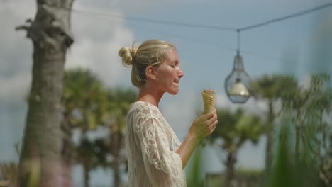 Bonita-Mujer-Rubia-Con-Un-Moderno-Vestido-Blanco-Tomando-Un-Bocado-De-Helado,-Vacaciones