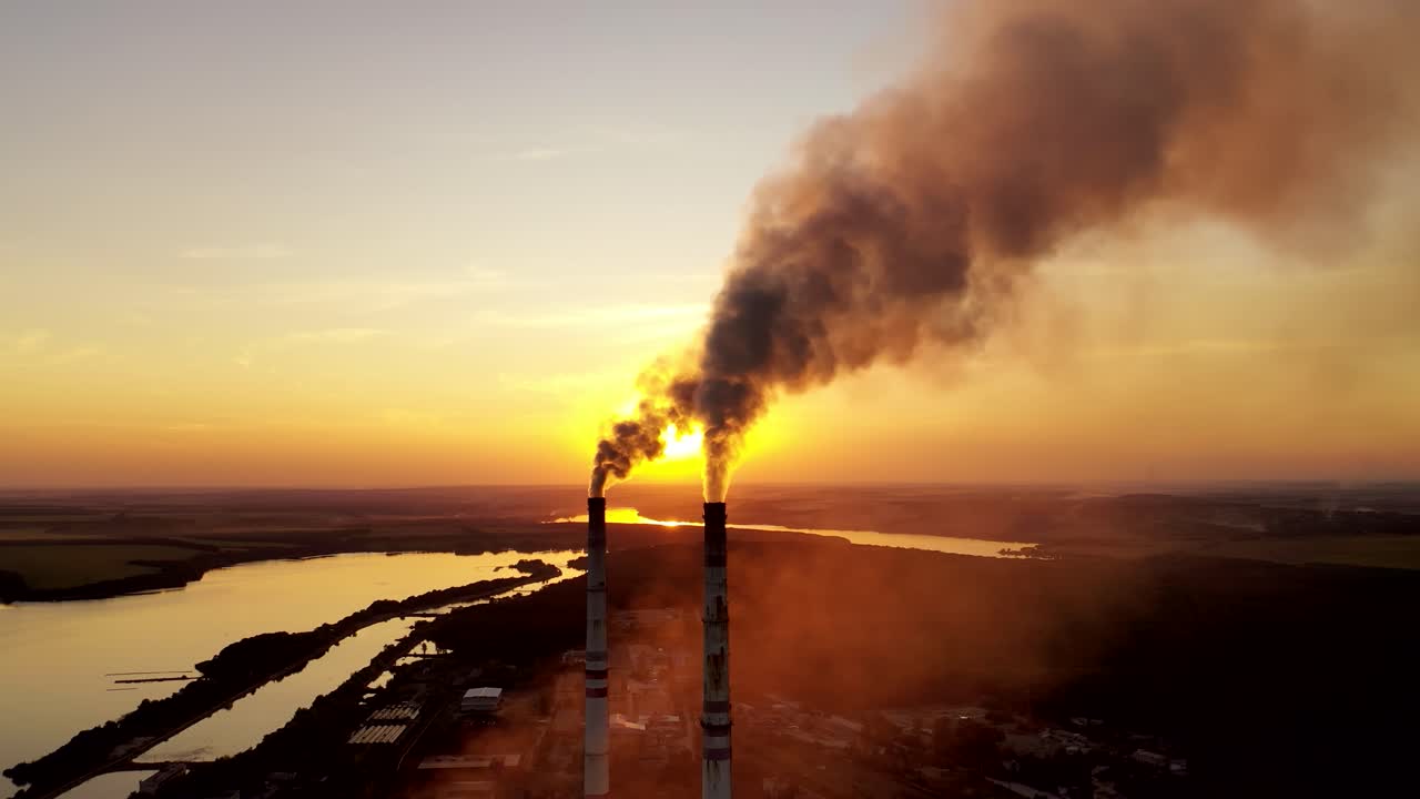 Industrial factory in natural landscape. Dirty smoke in the air at sunset. Large pipes of industrial factory produce chemical smoke in the evening. Environmental pollution.