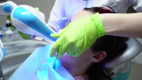 young woman with an expander in mouth and red protective glasses getting uv whitening at the dentist's office