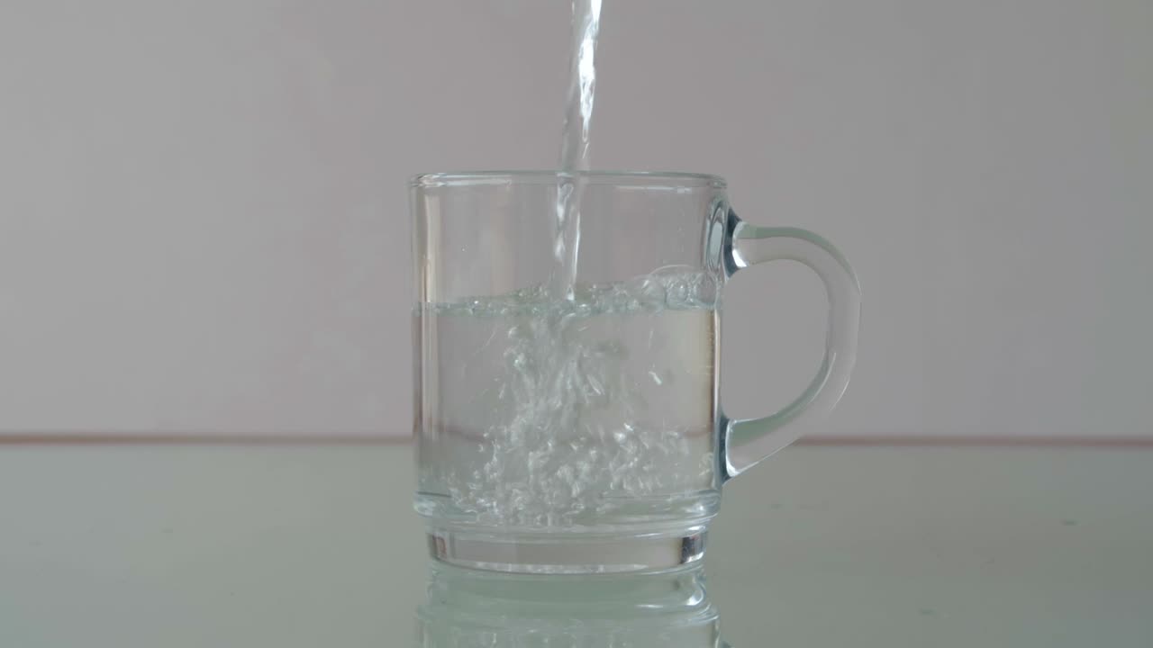 verter agua en un vaso de vidrio sobre la mesa con reflejo, todavía un primer plano en una configuración minimalista