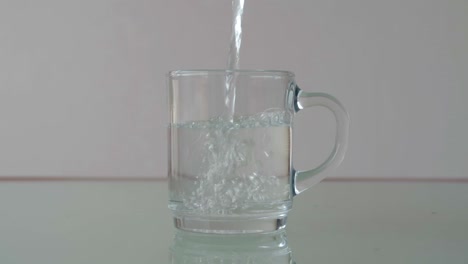 Pouring-water-in-glass-cup-on-table-with-relfection,-still-close-up-shot-in-minimalist-setup