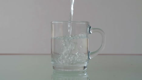 verter agua en un vaso de vidrio sobre la mesa con reflejo, todavía un primer plano en una configuración minimalista
