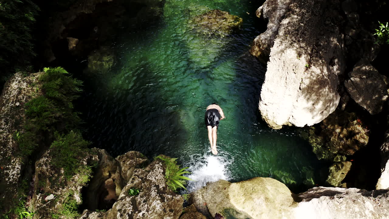 Person swimming in a crystal clear waterfall in a jungle setting