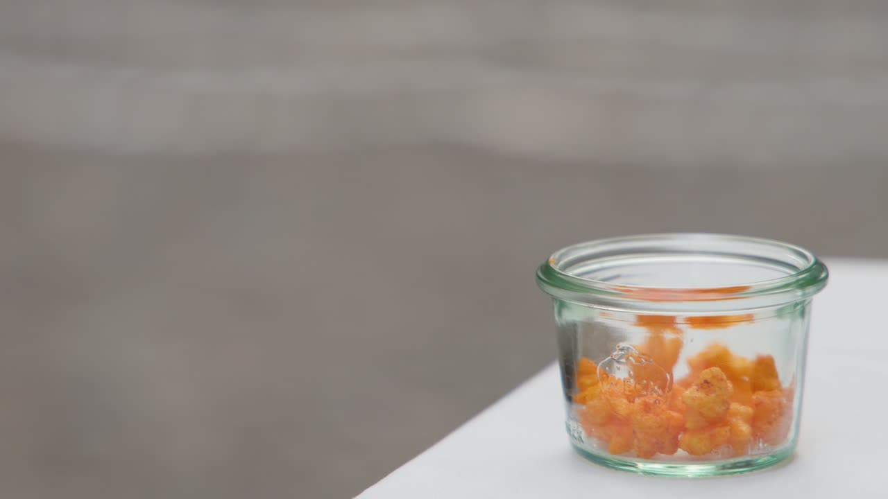 Hand reaching into a glass jar of popcorn on a white table outdoors in daylight