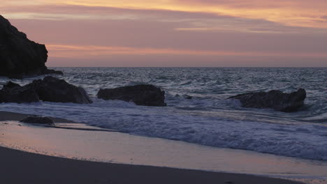 Wunderschöne-Strandlandschaft-Bei-Sonnenuntergang-Mit-Wellen,-Klippen-Im-Hintergrund-Bei-Ebbe