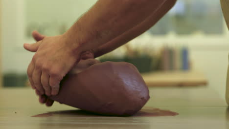 male hands placing raw clay material onto studio work table preparing top sculpt block