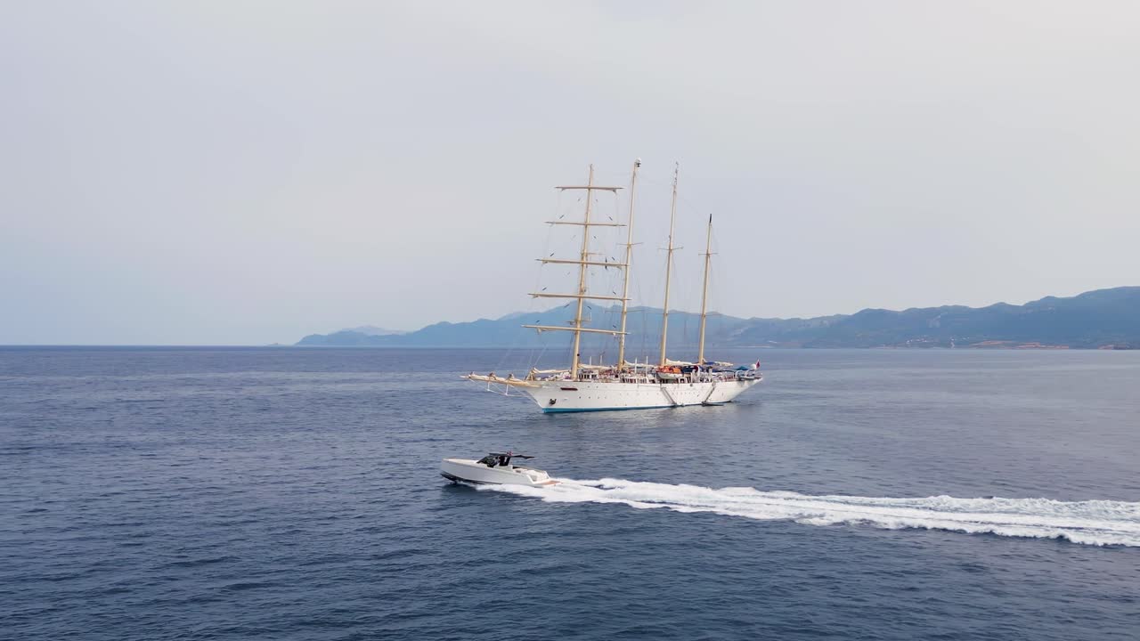 Drone captures a sleek speedboat cruising past a majestic four-masted sailing ship on open sea, blending modern design with nautical tradition