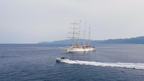drone captures a sleek speedboat cruising past a majestic four-masted sailing ship on open sea, blending modern design with nautical tradition