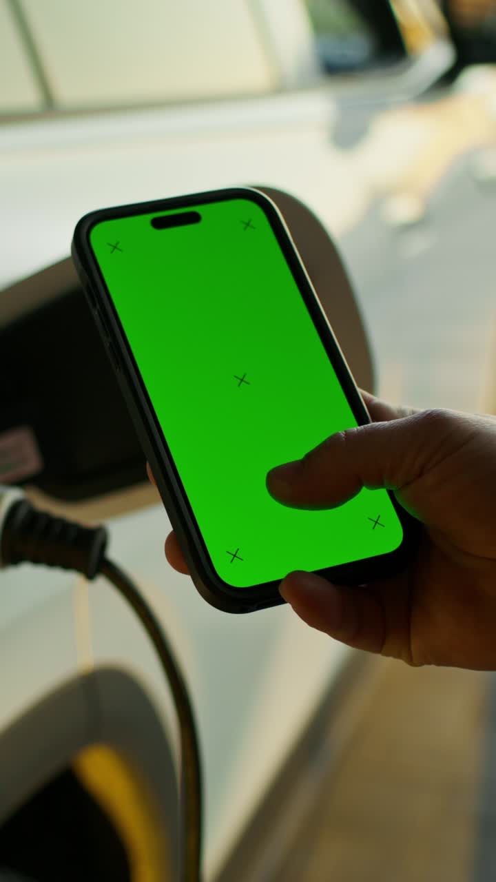 persona que utiliza un teléfono inteligente mientras carga un vehículo eléctrico