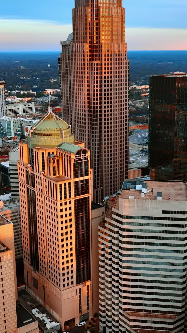 Luz alaranjada do pôr do sol nas fachadas dos arranha-céus. Vista do centro de Charlotte, Estados Unidos, de cima. Vídeo vertical.