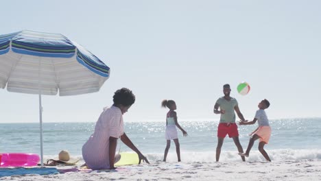 happy african american family playing ball, having fun on beach