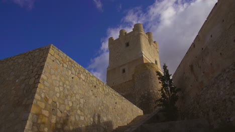 low angle view of the atalaya castle where clouds are moving under the blue sky, villena, province of alicante, southern spain