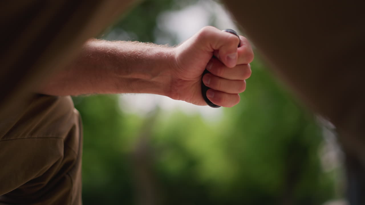Seated Man Practicing Wrist Mobility, Natural Setting Of Man Gripping Ring During Steady Wrist Exercise, Closeup View Of Community Member Practicing Wrist Movement In Green Outdoor Environment