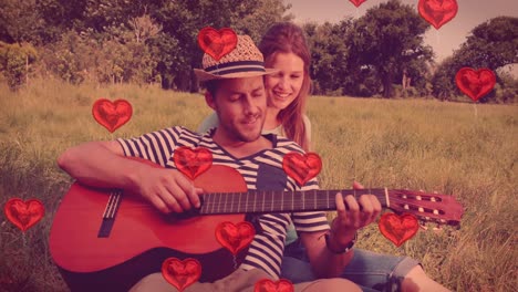 multiple heart balloons floating against man playing guitar for his woman in the woods