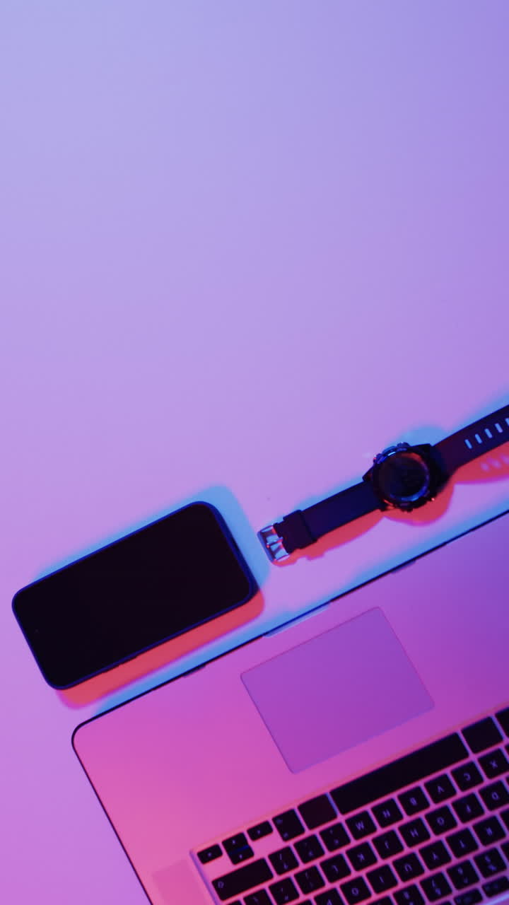 Vertical video of laptop, smartphone and smartwatch on purple neon background