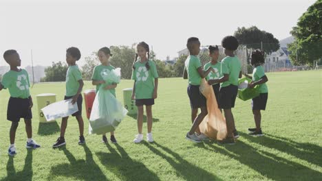 Fröhliche,-Vielfältige-Schulkinder-Tragen-Recycling-T-Shirts-Und-Reinigen-Den-Sportplatz-In-Der-Grundschule