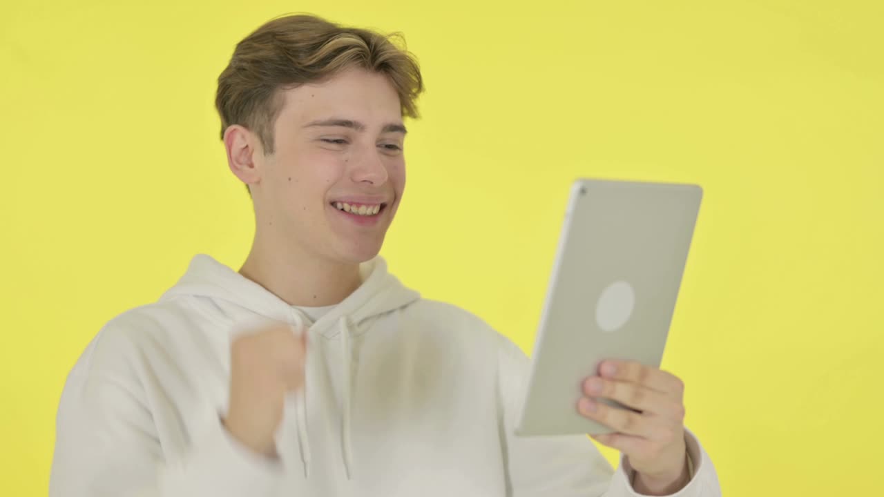 노란색 배경의 태블릿에서 성공을 축하하는 젊은 남자