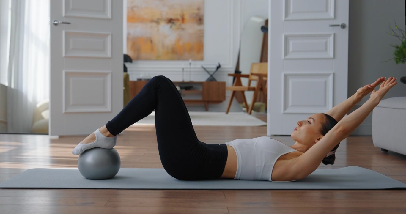 Young Woman Doing Pilates Core Workout with Exercise Ball at Home