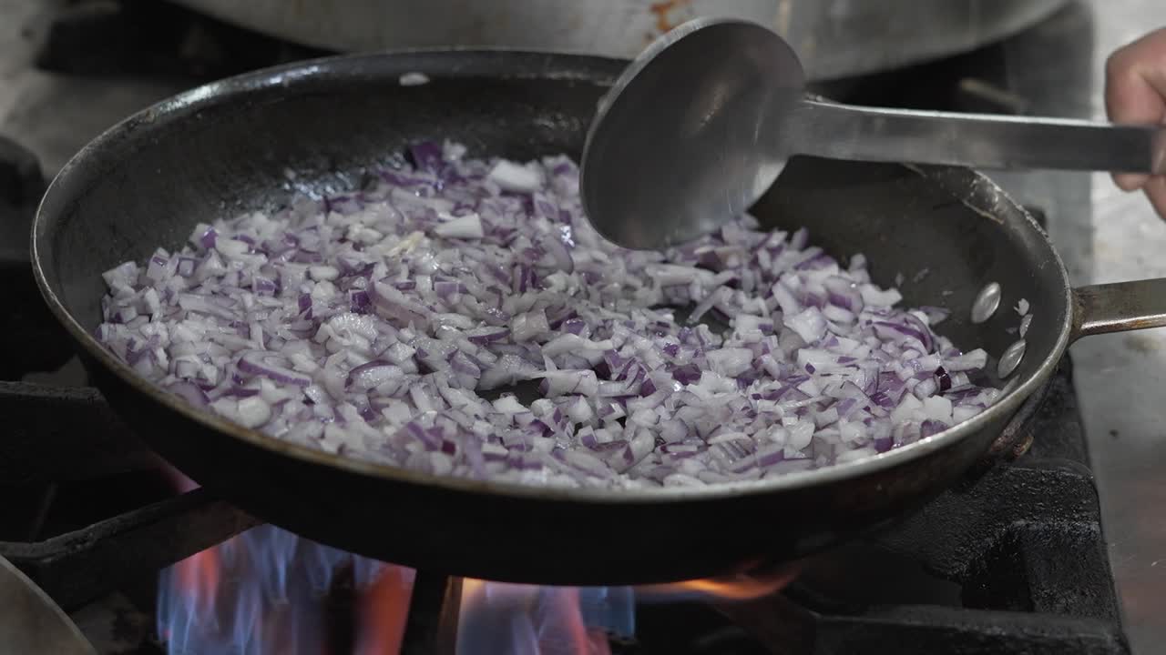 Chopped red onions sautéing in a pan over a gas flame, cooking process in action, kitchen setting
