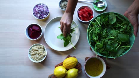 Aerial-shot-of-adding-spinach-leaves-to-plate-of-salad-making-of-a-salad-adding-tomatoes-carrots-spinach-chick-peas-lemons-onions-nuts-dressing-in-view