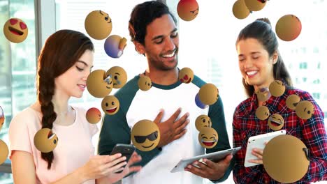 Multiple-face-emojis-floating-against-office-colleagues-discussing-over-digital-tablet