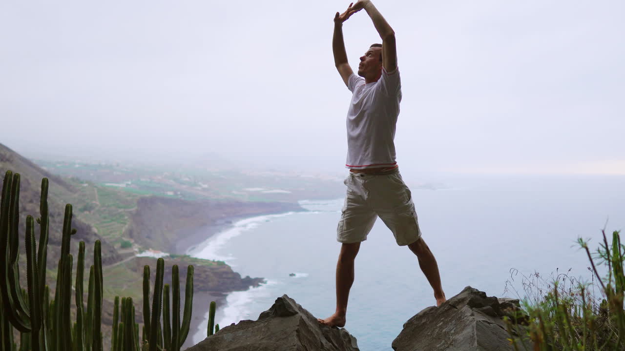 un joven realiza yoga de saludo al sol en una montaña, con vistas al océano. él disfruta de la meditación y el yoga, encarnando el fitness, el deporte y un estilo de vida saludable