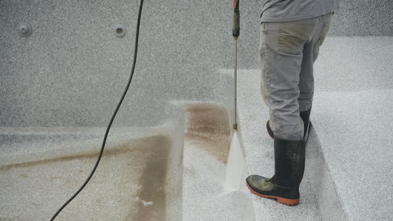 Worker power washes dirty pool steps before fiberglass pool installation