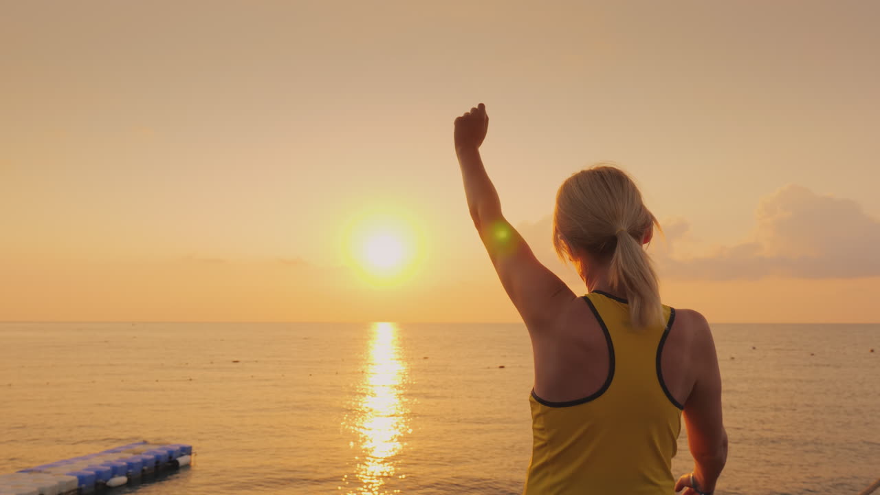 Donna di mezza età che si riscalda sul molo, con lo sfondo di una bellissima alba sul mare.