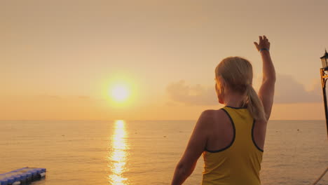 Mujer-De-Mediana-Edad-Calentando-En-El-Muelle-En-El-Fondo-De-Un-Hermoso-Amanecer-Junto-Al-Mar