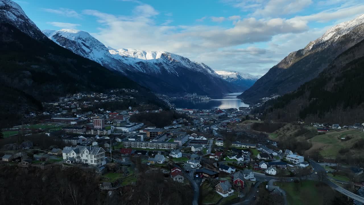 Odda Norway in the evening with full cityscape, Sorfjorden, and towering mountains. Snow capped peaks lit by sunset