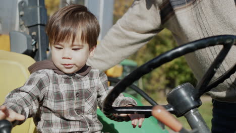 baby farmer playing behind the wheel of a tractor, next to his father