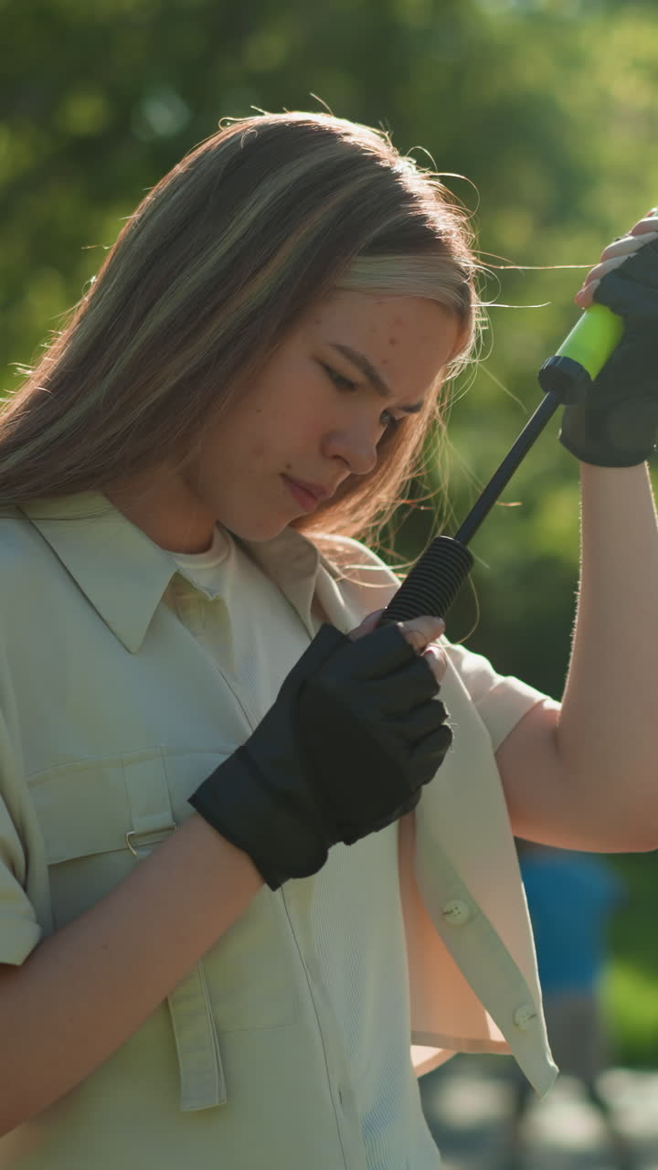 금발 머리카락을 가진 젊은 소녀는 야외에 서서, 사려 깊게 녹색 공기 프 손잡이를 조사, 파란 셔츠와 빨간 헬 롤러 스케이트 소년은 부드러운 초점