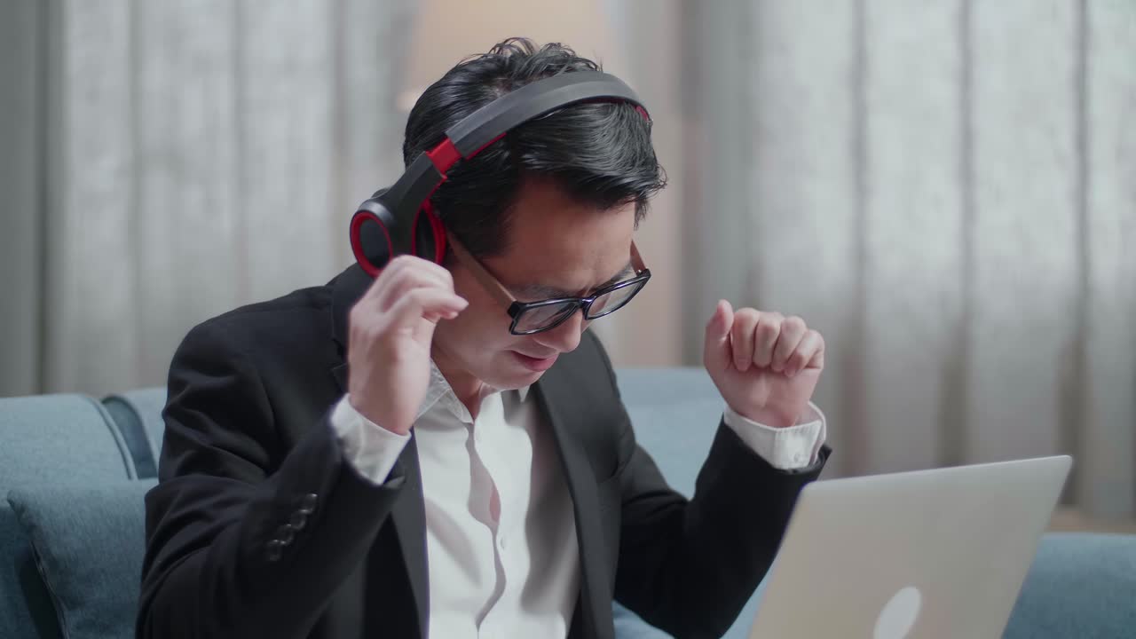 집에서 노트북으로 일하면서 헤드폰으로 음악을 듣고 춤을 추는 재과 쇼트를 입은 아시아 사업가